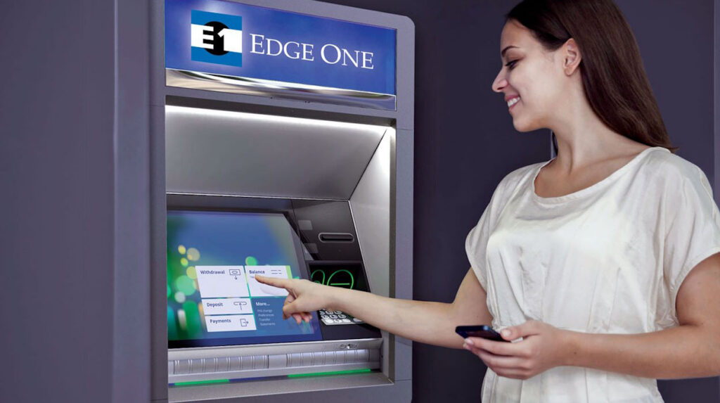 Woman smiling while using an ATM touchscreen showing options for withdrawal, balance, deposit, payments, and more