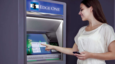 Woman smiling while using an ATM touchscreen showing options for withdrawal, balance, deposit, payments, and more